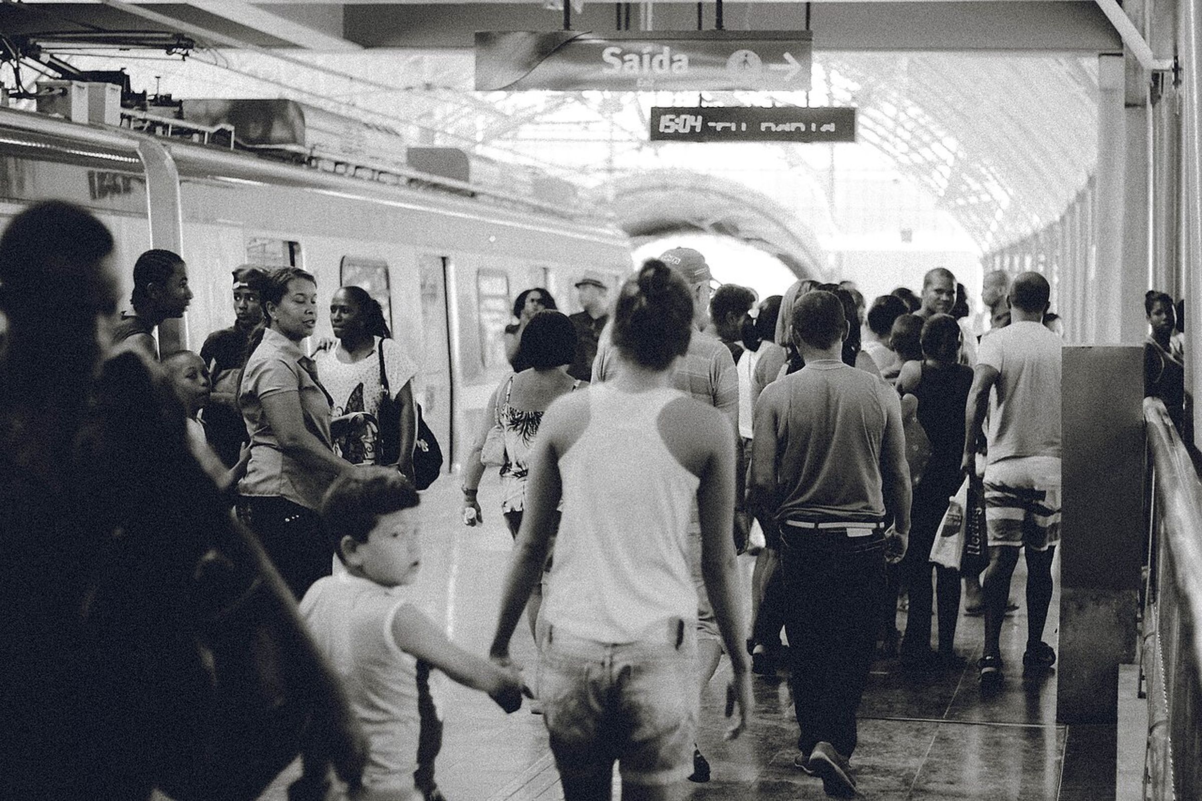 A crowd of people walking through a railway station passage, photographed in black and white
